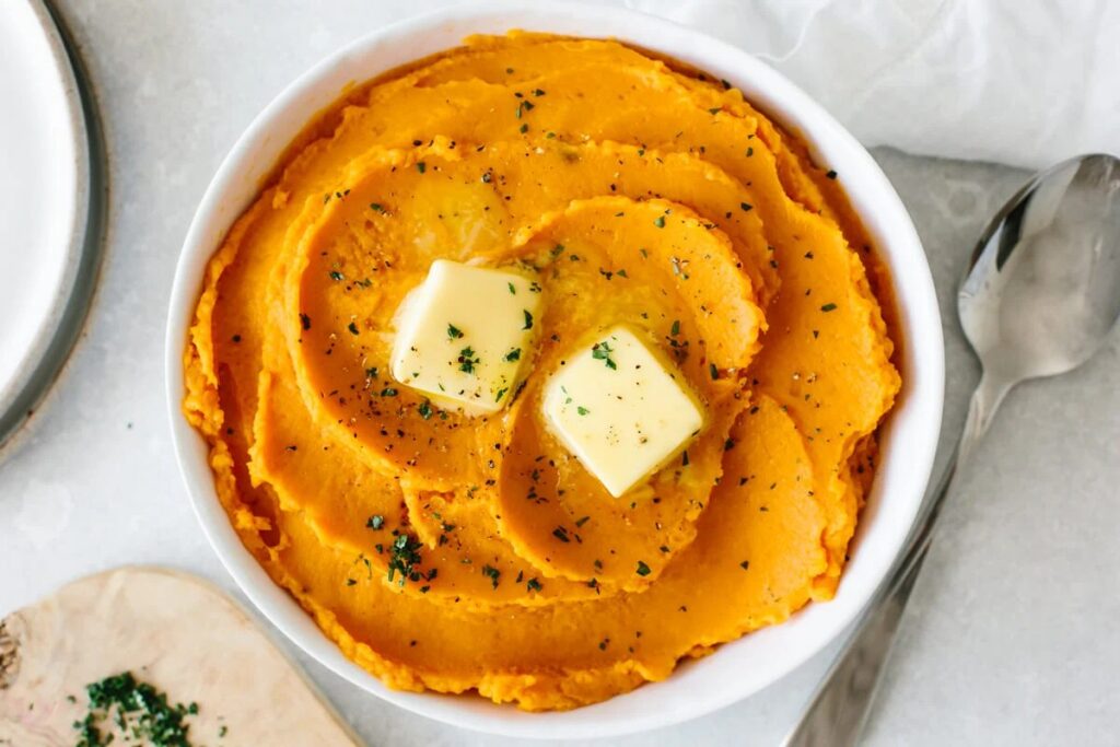 Mashed sweet potatoes in a white bowl topped with butter.